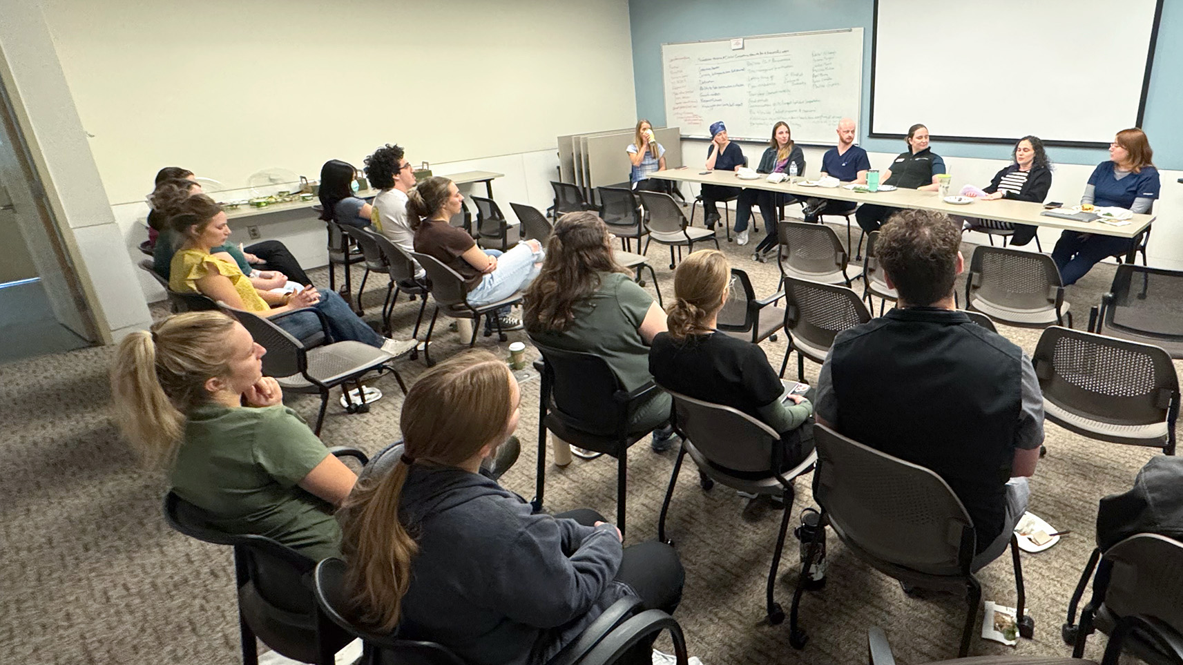 Classroom with two rows of students seated in chairs looking at panel of faculty and staff sitting at a table in the front of the room during a STAR program panel discussion.